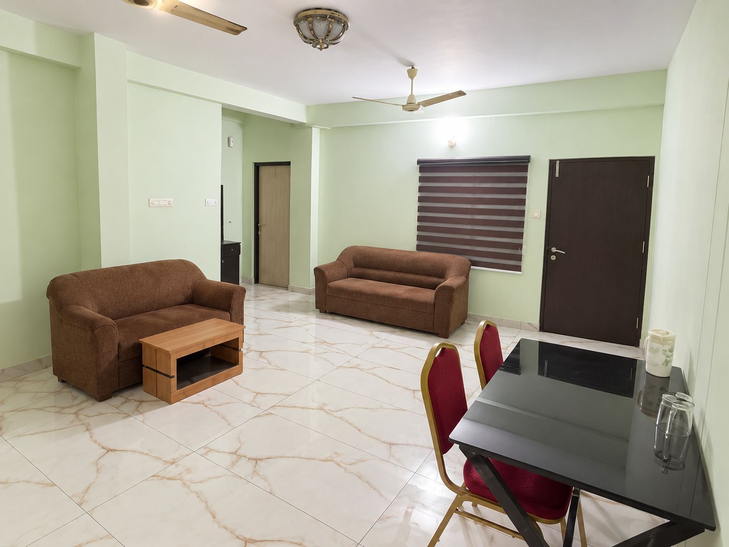 Living hall of a family apartment at Safalyam Residency, with two sofas, a dining table and marble floors